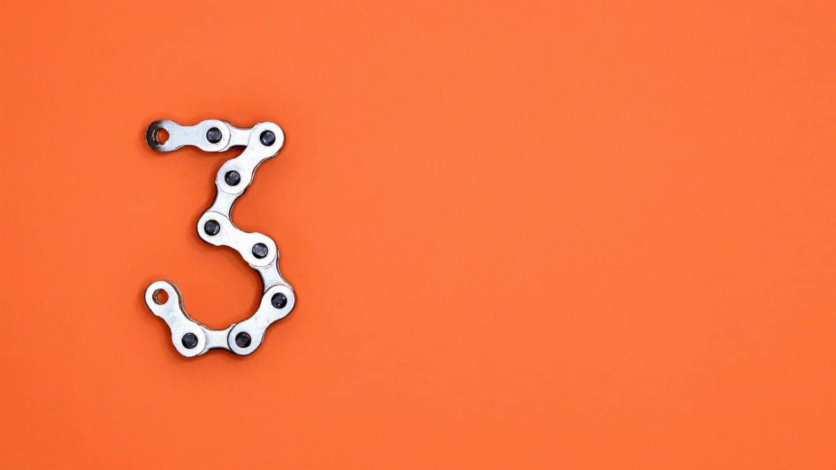 A bicycle chain forms the number three against a vibrant orange backdrop, offering ample copyspace.