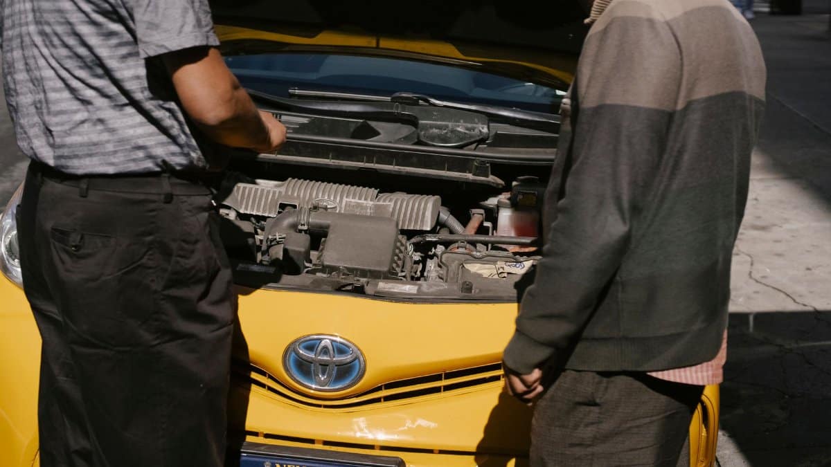 Back view of crop anonymous males checking details of engine under hood of cab in New York