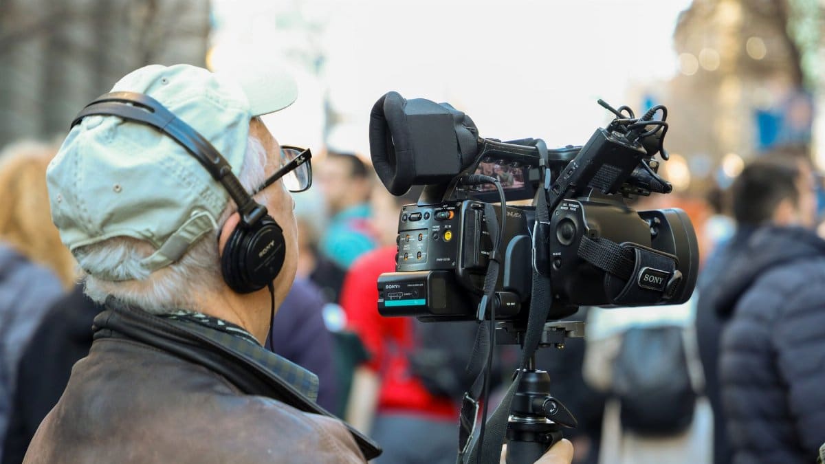 A cameraman records an urban event with professional equipment in a bustling city setting.