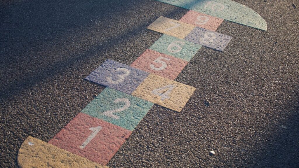 A vibrant hopscotch grid painted on an outdoor playground surface, lit by daylight.
