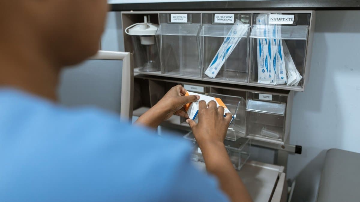 A nurse organizes medical supplies in a hospital setting. Focus on hands and storage unit with IV kits.