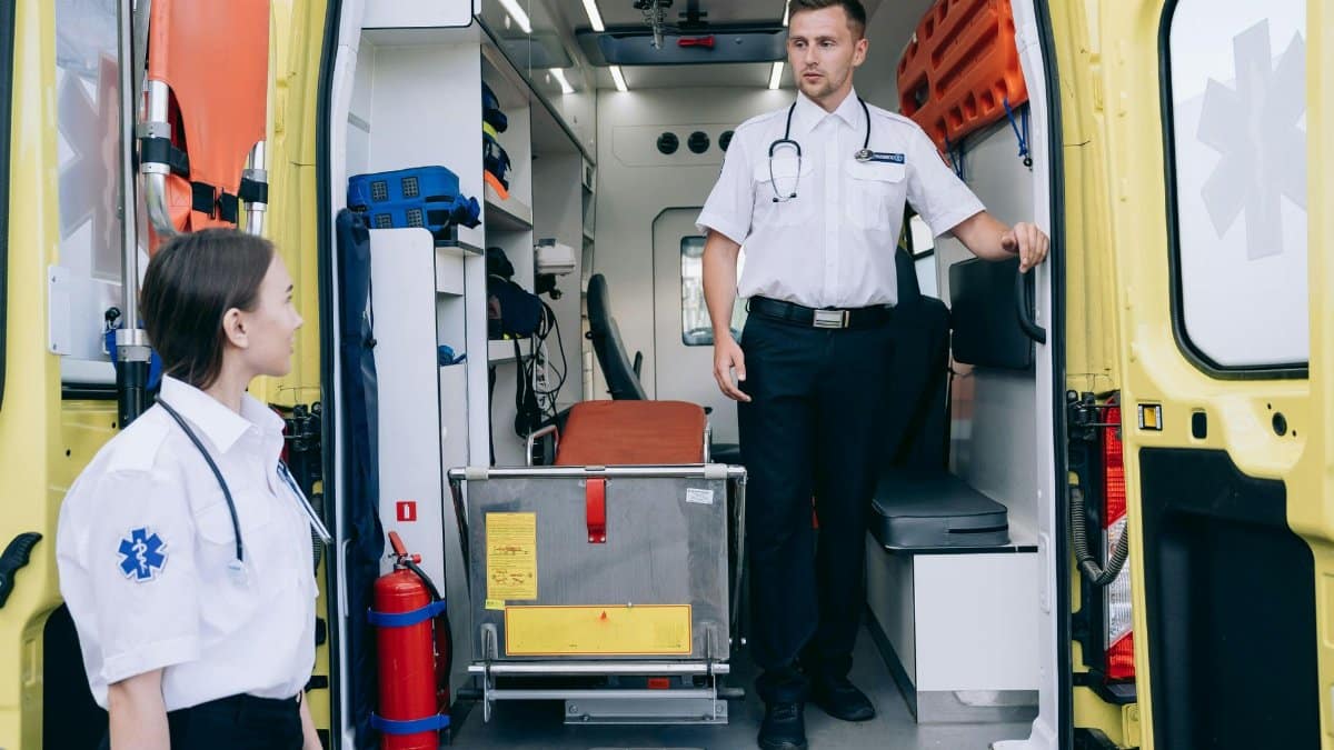 Two paramedics in uniforms and stethoscopes preparing ambulance for upcoming medical emergencies.
