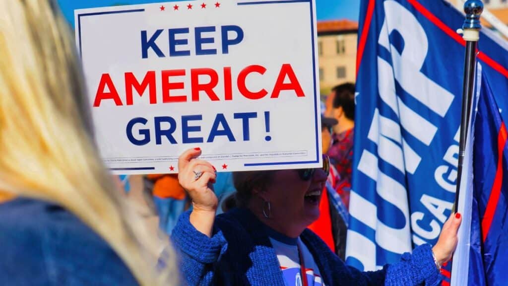 Crowd gathering in Phoenix holding 'Keep America Great' sign at political event outdoors.
