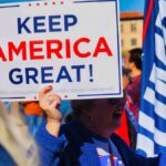 Crowd gathering in Phoenix holding 'Keep America Great' sign at political event outdoors.