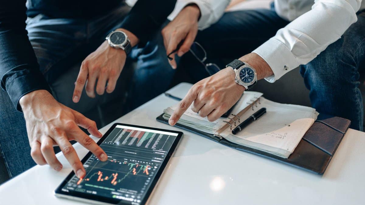Two businessmen discussing financial data on a tablet during a meeting.