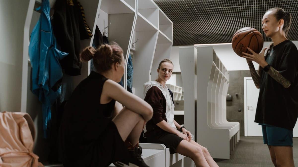 Three women basketball players chatting in a modern locker room setting.
