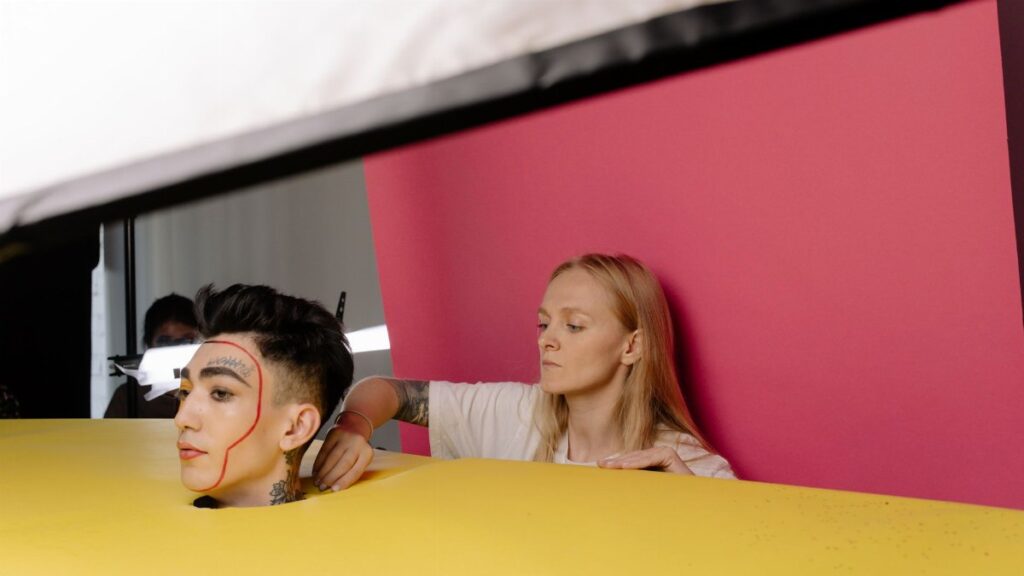 A behind-the-scenes look at a studio photoshoot featuring a model with unique makeup artistry and vibrant background.
