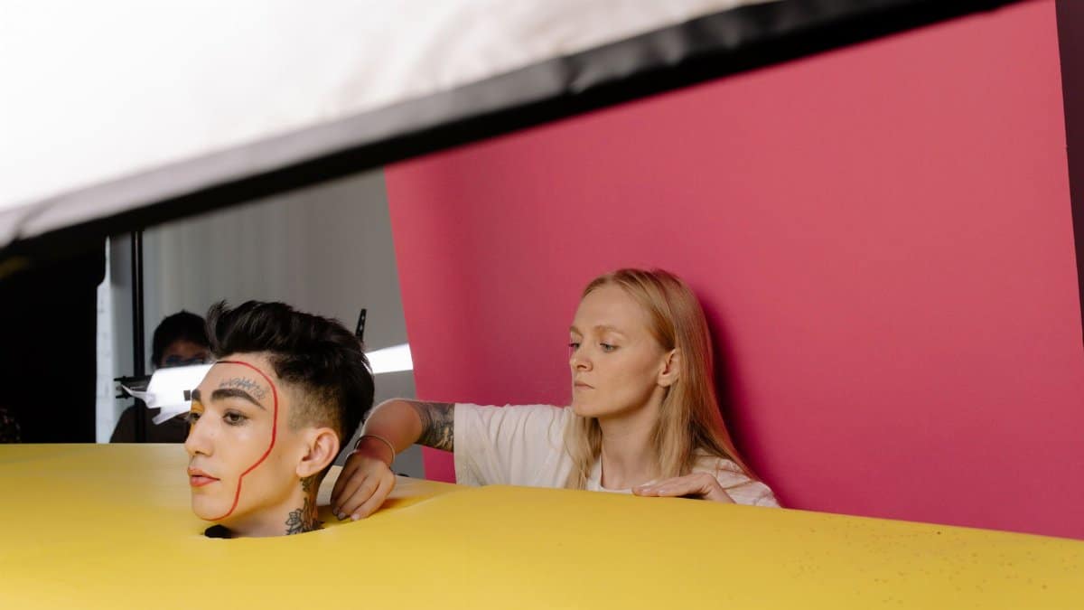A behind-the-scenes look at a studio photoshoot featuring a model with unique makeup artistry and vibrant background.