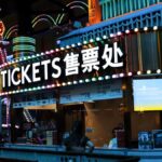 Illuminated ticket booth with vibrant neon lights at night, featuring colorful signage.