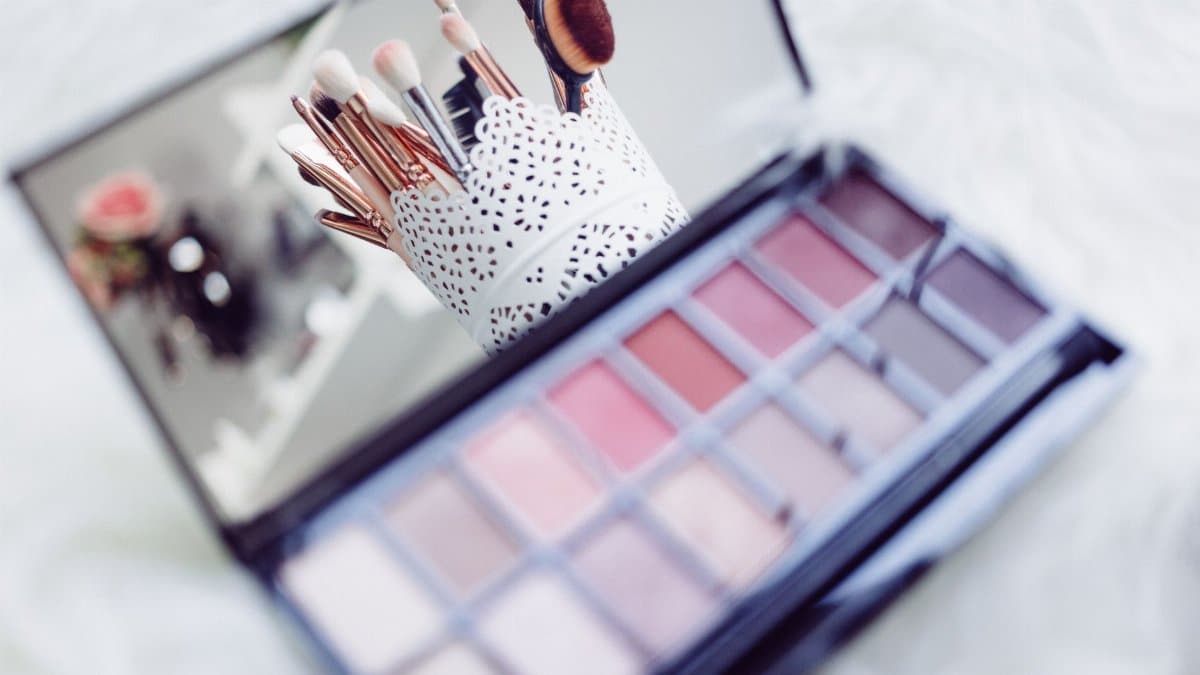 Close-up of makeup brushes in a decorative holder and a colorful eyeshadow palette.