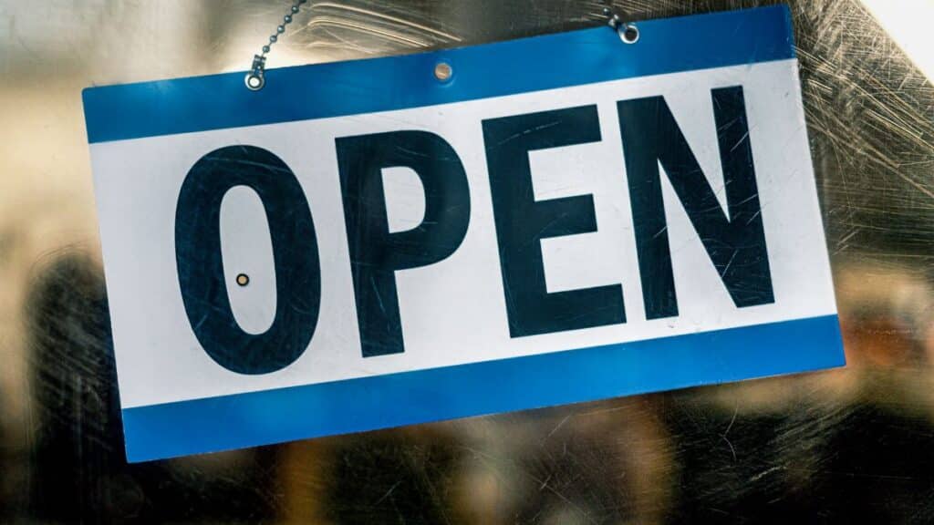 A blue and white open sign hanging on a retail shop's glass door.