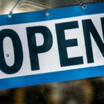 A blue and white open sign hanging on a retail shop's glass door.