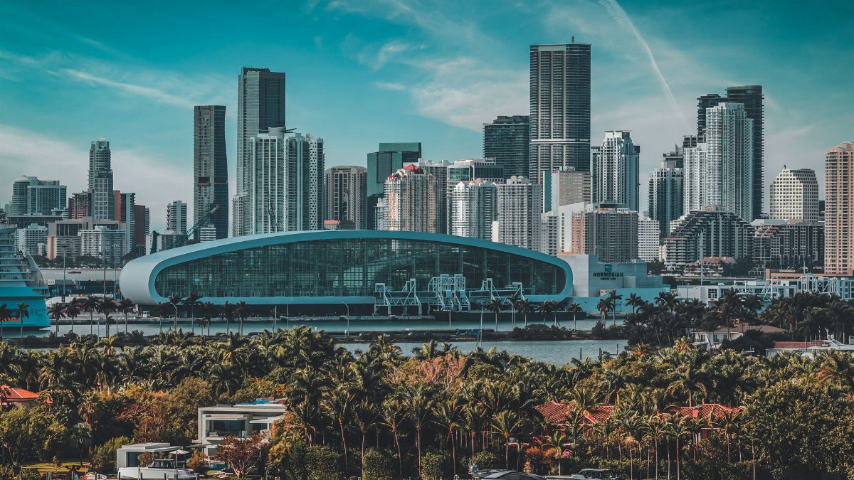 Scenic view of Miami skyline with modern skyscrapers and waterfront palm trees under blue skies.