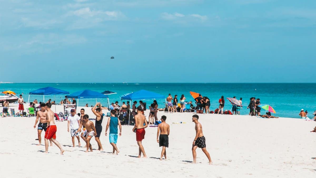 Crowds enjoy a sunny summer day at Miami Beach with clear blue skies and white sand.