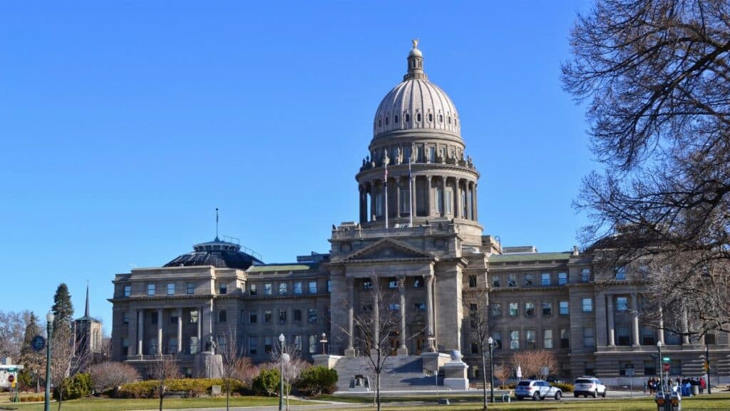 The Idaho State Capitol Building stands majestically under a clear blue sky with surrounding gardens.