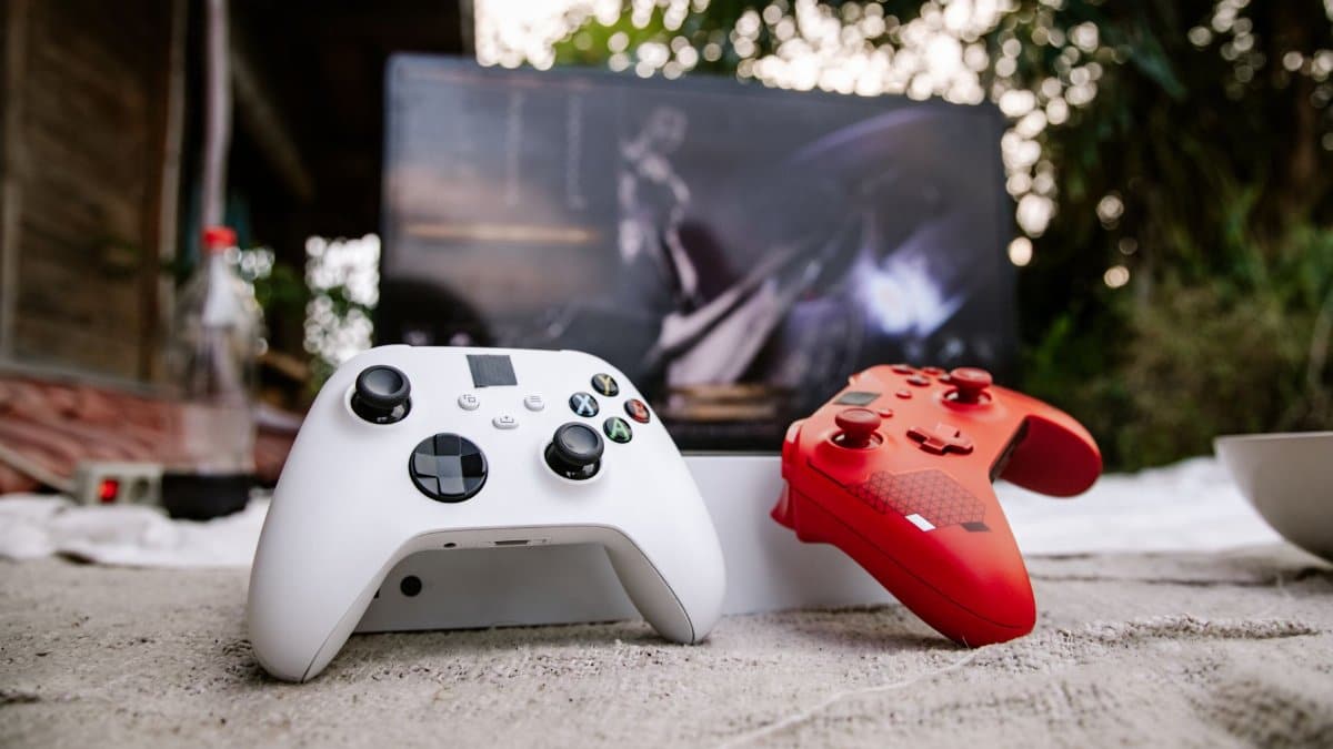 White and red Xbox wireless controllers set outdoors. A computer screen is blurred in the background.