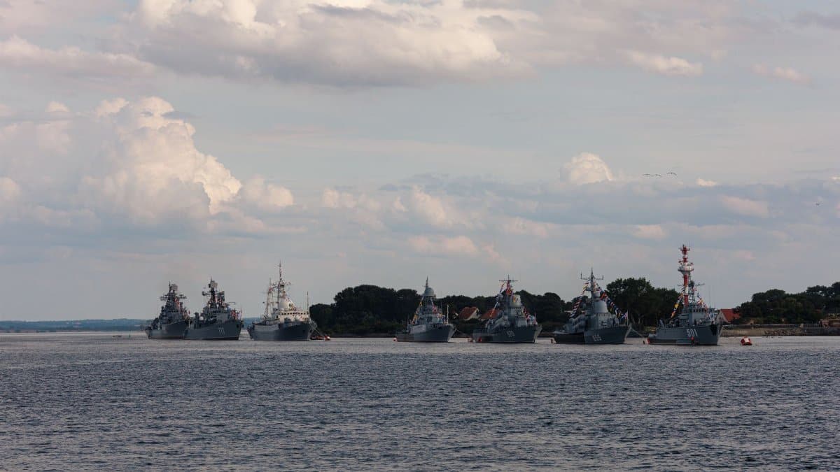 A fleet of military ships anchored with a cloudy sky backdrop.