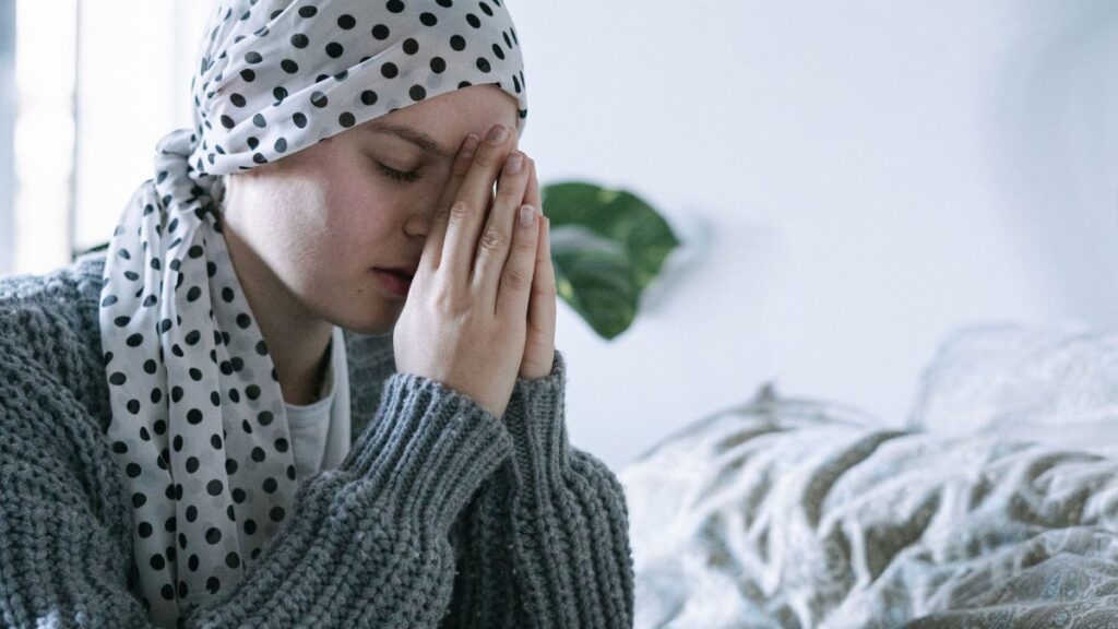 A woman wearing a scarf prays indoors, symbolizing hope and recovery from cancer.