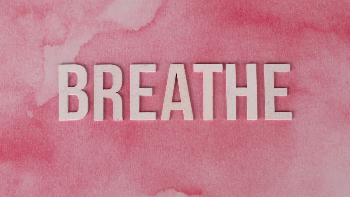 Motivational 'Breathe' text on a pink watercolor background, promoting relaxation and mindfulness.