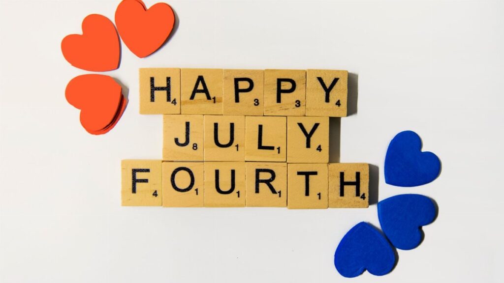 Flat lay of Scrabble tiles spelling 'Happy July Fourth' with colorful hearts, celebrating Independence Day.
