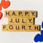 Flat lay of Scrabble tiles spelling 'Happy July Fourth' with colorful hearts, celebrating Independence Day.
