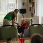 Caregiver assisting elderly women with tea in a cozy nursing home setting.
