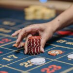 A hand holding poker chips on a roulette table, showcasing gambling and casino gaming.