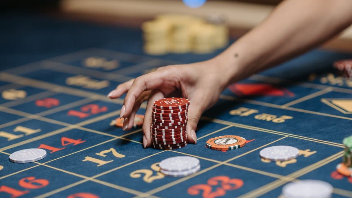 A hand holding poker chips on a roulette table, showcasing gambling and casino gaming.