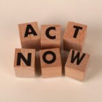 Wooden blocks with letters spelling 'ACT NOW', promoting urgency and motivation.