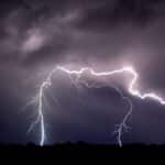 Vivid lightning bolts illuminate the dark night sky over an open field creating a striking natural display.