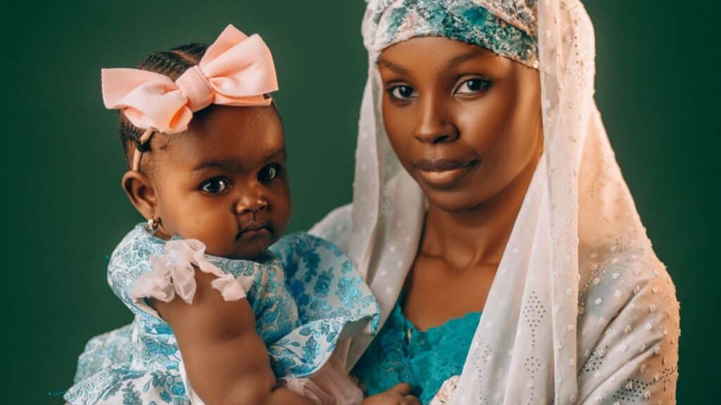A mother lovingly holds her baby, both dressed in vibrant traditional Nigerian attire.
