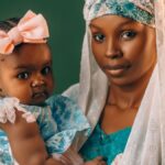 A mother lovingly holds her baby, both dressed in vibrant traditional Nigerian attire.