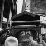 Crowd gathered for a traditional funeral procession in grayscale.