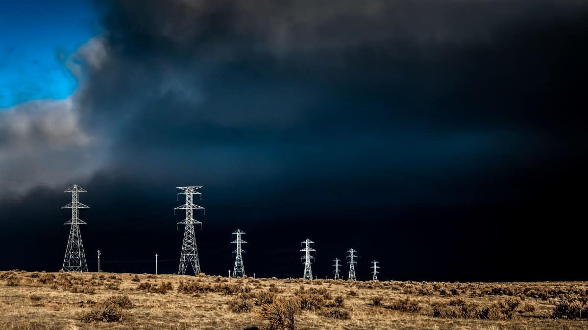 Power lines standing tall against dark storm clouds with a dramatic sky and open field.