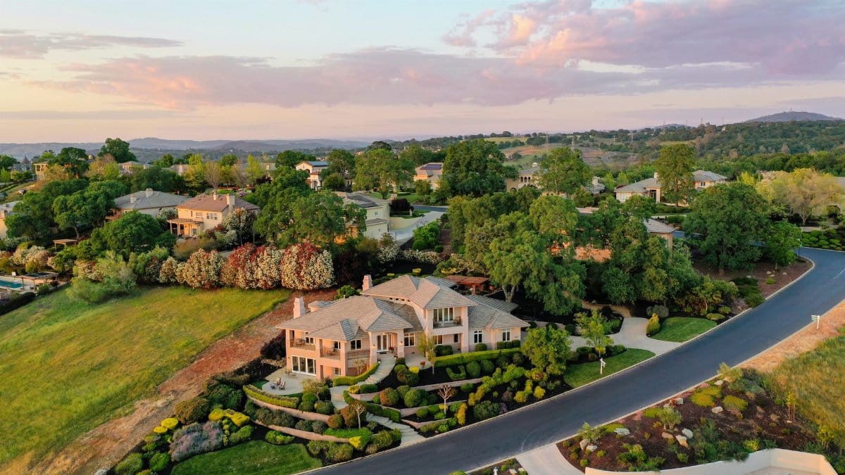 Aerial shot of elegant suburban houses with lush gardens during sunset.