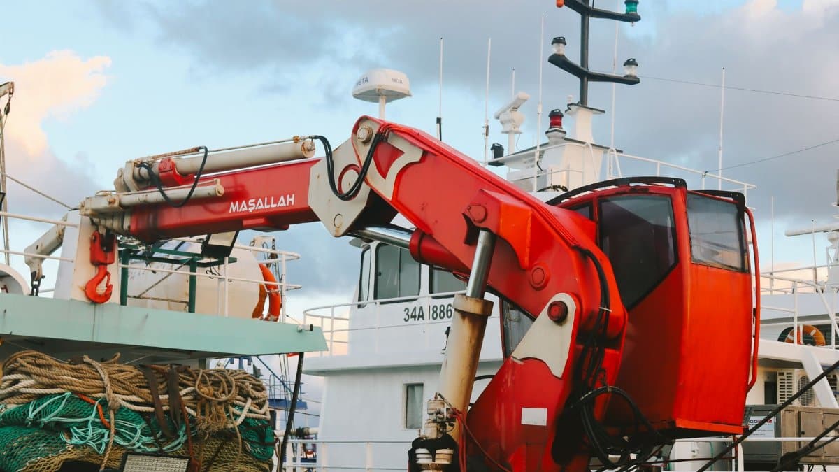 Red crane on an industrial fishing boat docked at the harbor with fishing nets.