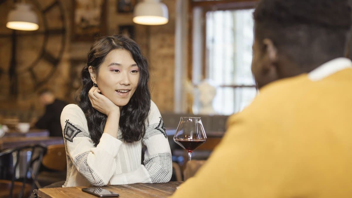 Two adults enjoying a conversation over wine in a warm, cozy café atmosphere.
