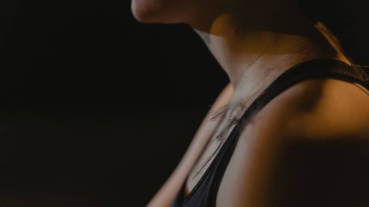 Close-up of a woman's neck wearing a tank top in low light, creating a moody atmosphere.