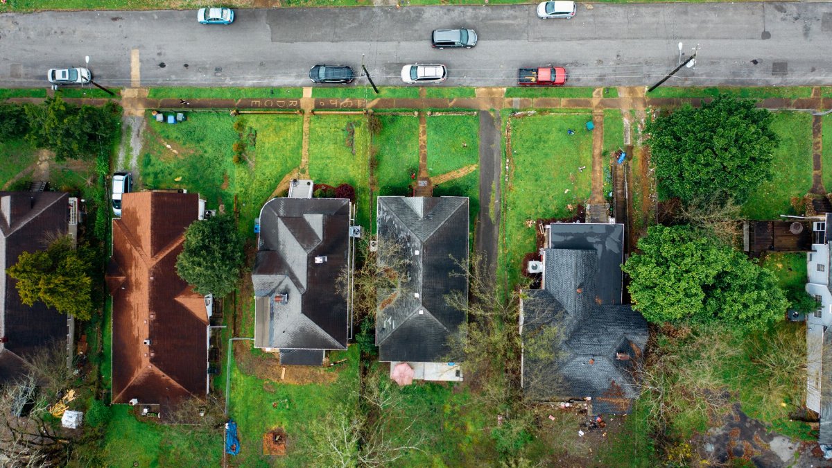 Drone shot capturing rooftops, greenery, and cars on a quiet urban street.
