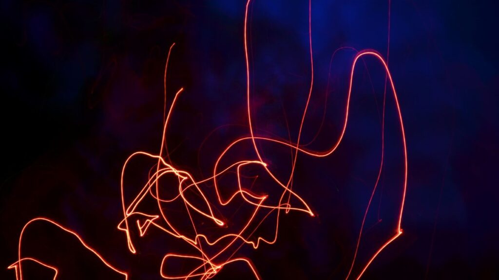 Vibrant neon light trails forming abstract patterns in a dark setting, creating a dynamic visual effect.