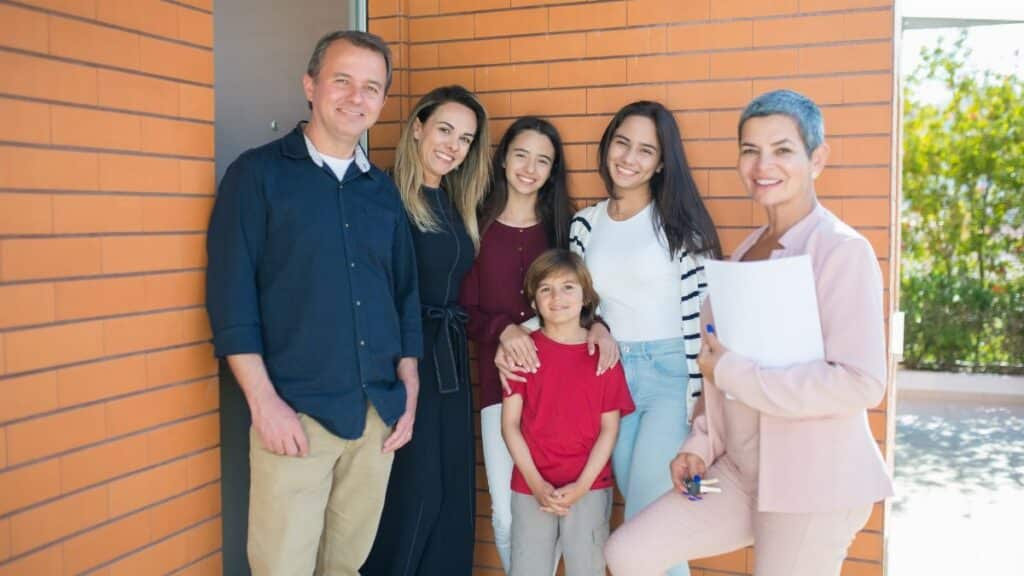 Smiling family with a realtor standing outside their new home, celebrating together.