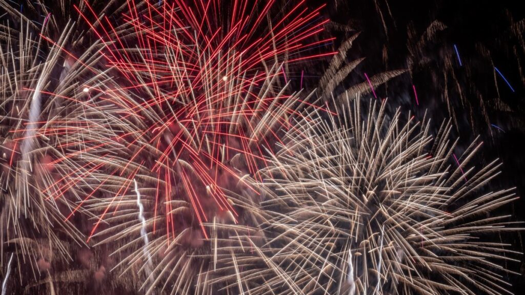 Vibrant fireworks illuminate the night sky with red and white bursts, celebrating a festive occasion.