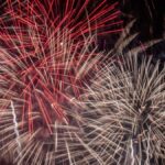 Vibrant fireworks illuminate the night sky with red and white bursts, celebrating a festive occasion.