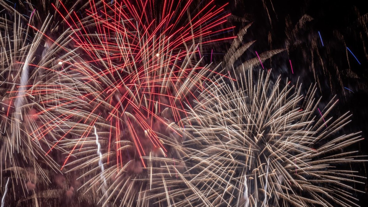 Vibrant fireworks illuminate the night sky with red and white bursts, celebrating a festive occasion.