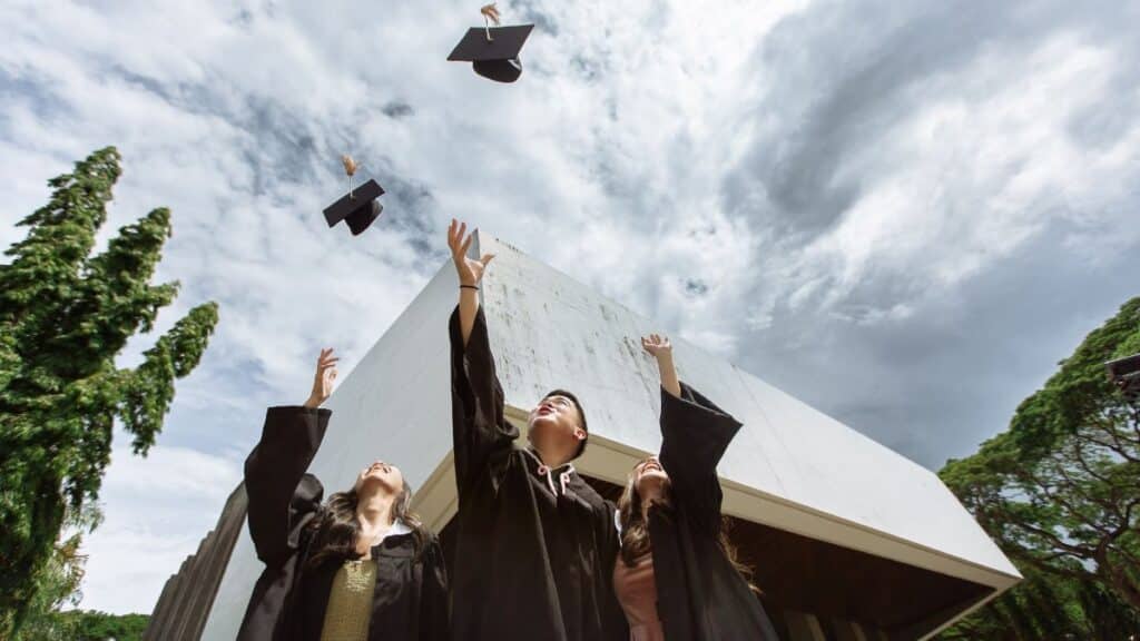 Graduates joyfully tossing caps in air outdoors against a modern building.