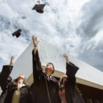Graduates joyfully tossing caps in air outdoors against a modern building.