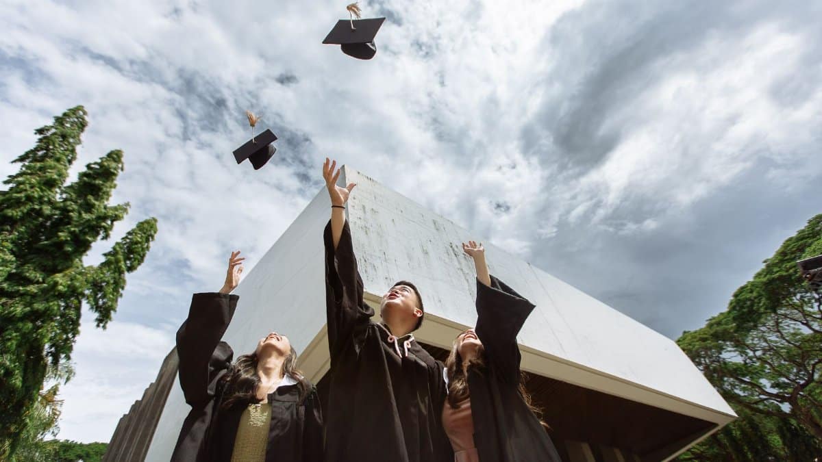 Graduates joyfully tossing caps in air outdoors against a modern building.