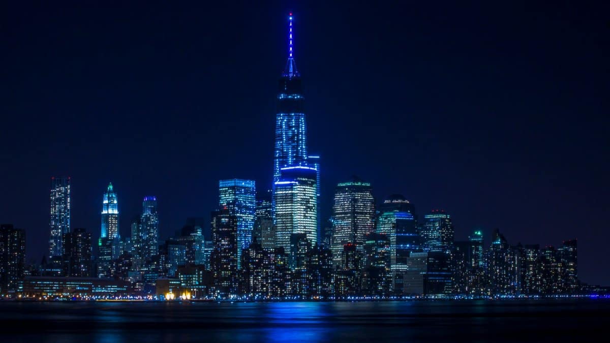 Illuminated New York City skyline reflecting over the Hudson River at night.