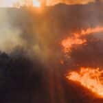 Aerial shot of a forest fire near White River, South Africa, showcasing dramatic flames and smoke at sunset.