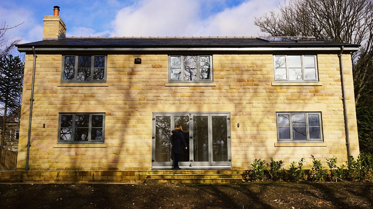 Contemporary brick house exterior with glass windows and a woman at the door in the UK.